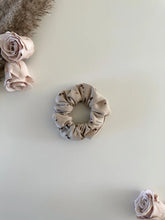 Load image into Gallery viewer, Baby scrunchie featuring a floral print on a ribbed beige fabric.