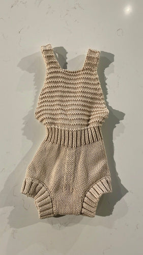 Knit beige romper with straps crossing in the back with buttons. 